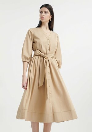 Vestido midi de algodón beige con escote en V, delantero abotonado y mangas abullonadas con elástico, cintura ajustada con un cinturón y una textura suave.