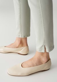 Ballerine in pelle beige con punta tonda e tacco basso, abbinate a pantaloni verde chiaro alla caviglia con spacchi laterali ai polsini.