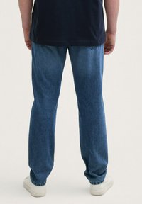 Vaqueros de denim azul con corte recto, con un lavado claro y detalles de costura sutiles, combinados con zapatillas blancas.