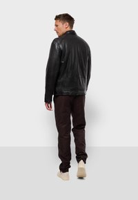 Black leather jacket with a collar, displayed from the back. The jacket features a smooth texture and subtle stitching details, paired with brown pants.