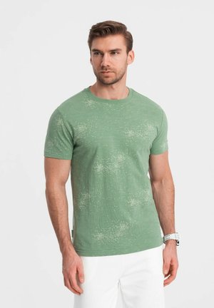 Camiseta verde de manga corta con un patrón texturizado y sutiles motitas, cuello redondo y un corte holgado, combinada con pantalones blancos.