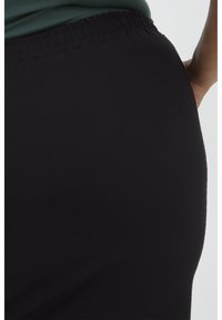 Zwarte, rekbare leggings van stof met een hoge tailleband. Gladde textuur, aansluitend ontwerp en eenvoudige silhouet zonder extra versieringen.