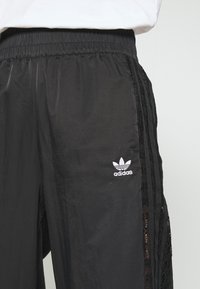 Svarta träningsbyxor med en texturerad spetspanel på sidan. Har en elastisk midja och en liten vit Adidas-logotyp på framsidan.