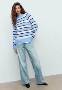 Maglione a righe azzurro chiaro con strisce blu navy e crema, abbinato a jeans a gamba larga in lavaggio chiaro e scarpe nere con punta a punta.