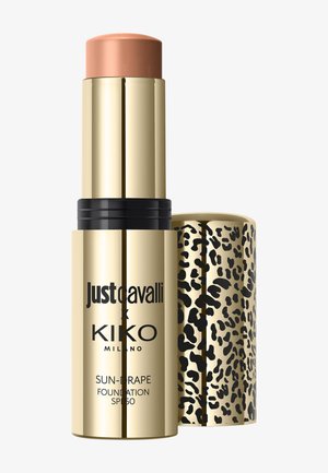 Gouden foundation-stick met beige make-uptip, zwarte tekst en een afneembare gouden luipaardprintdop op een witte achtergrond.