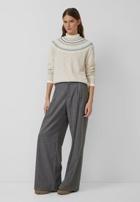 Beżowy sweter z wzorzystym dekoltem i długimi rękawami, zestawiony z wysokim stanem, szerokimi spodniami w szare pasy. Miękka tekstura i luźny krój.