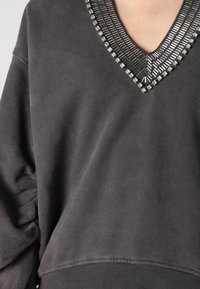 Sweatshirt gris avec un décolleté en V profond, présentant des clous en argent décoratifs autour du col et un tissu texturé et doux.