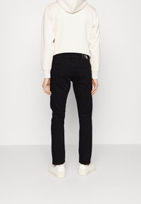 Svarta denimjeans med slim fit, bakfickor och ett tygmärke. Kombinerat med en ljusgrå hoodiesweatshirt och vita sneakers.