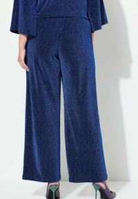 Pantaloni a gamba larga blu con una finitura strutturata e scintillante, dotati di una vita elastica. Abbinati a scarpe con tacco nere e verdi.