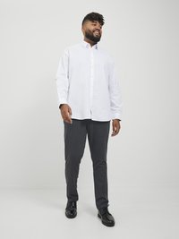 Camisa blanca de manga larga con botones, pantalones grises y zapatos negros. La camisa tiene un cuello extendido; los pantalones son de textura suave.