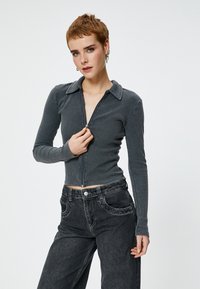 Grå ribbet zip-up trøje med lange ærmer og krave, parret med højtaljede mørke denim jeans. Simpelt, tætsiddende design uden mønstre.