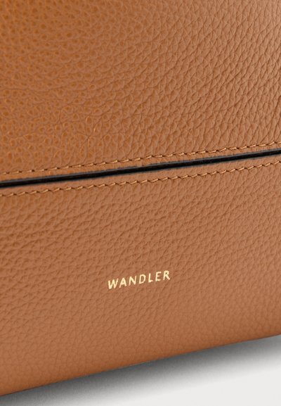 Tan-färgad läderväska med en guldfärgad "WANDLER"-logotyp, accentuerad med svarta sömmar. Slät yta med en subtil struktur.