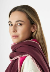 Écharpe bordeaux avec des accents roses, en tissu texturé et détail de couture contrastant le long des bords, drapée sur une épaule.