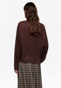 Bruine lange mouwen top met een losse pasvorm, met een afgeronde onderzoom, gecombineerd met een geruite rok in aardetinten en verschillende breedtes.