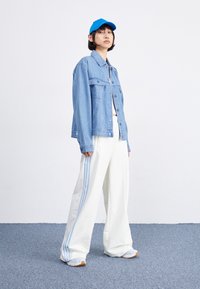 Vaaleansininen farkkutakki, jossa on kaksi rintataskua, valkoiset leveät housut, joissa on vaaleansinisiä raitoja, sekä sininen lippalakki.