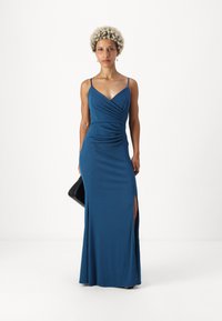 Vestido de noite longo e justo em azul-petróleo com alças finas, decote em V e fendas laterais. O tecido tem um padrão texturizado e um acabamento suave.