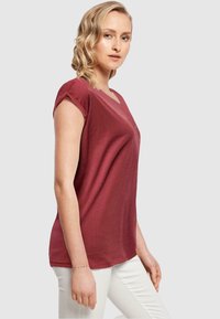 Mørkebrun V-hals T-shirt med korte rullede ærmer, blød tekstur, afslappet pasform og diskret syning, parret med lyse bukser.