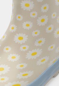 Beige rubber rain boot with white daisies and yellow centers. Features a light blue outsole and smooth, glossy texture.