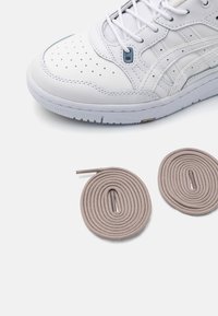 Hvite sneakers med perforert skinn, rund tå og lyseblå detaljer. To sammenrullede beige skolisser plassert under.
