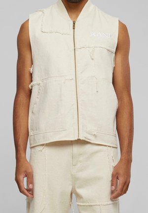 Ærmeløs off-white denimvest med forrest lynlås, flossede kanter, lappelommer, båret af en person med matchende off-white flossede bukser.