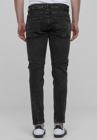 Jeans de mezclilla elástica negra con corte ajustado, que cuentan con cinco bolsillos y costuras clásicas. Combinados con zapatillas blancas y negras.