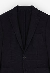 Blazer oscuro tejido con solapas en pico. Tiene dos botones frontales, un bolsillo en el pecho y una tela texturizada. El color es un azul marino profundo.