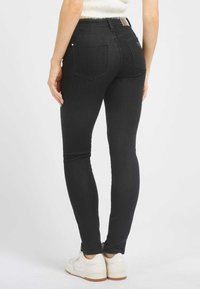 Černé skinny džíny s vysokým pasem, bezšvové zadní kapsy a hladkou texturou, v kombinaci s bílými teniskami.
