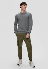 Pull gris à manches longues, col rond ; pantalon cargo olive avec poches latérales et bas fuselés ; baskets blanches avec accents gris.