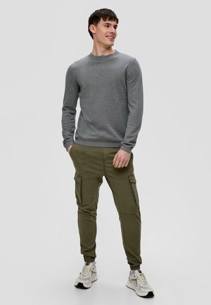 Grauer Pullover mit langen Ärmeln, runder Ausschnitt; olivfarbige Cargo-Hosen mit Seitentaschen und schmal zulaufenden Säumen; weiße Sneakers mit grauen Akzenten.