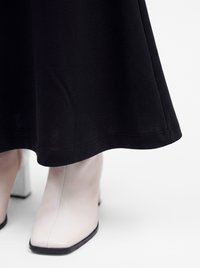 Bottes blanches en cuir à bout pointu portées avec une longue jupe noire, vues de face sur fond blanc.