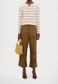 Beige ribbad cardigan med blå ränder, ihopparad med bruna vida byxor och svarta klacksandaler. Håller en vävd gul handväska.