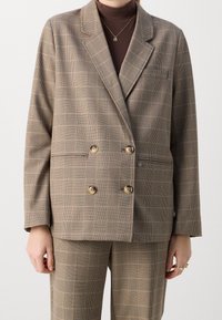 Hnědý kostkovaný dvouřadý blazer se dvěma předními kapsami a zlatými knoflíky, v kombinaci se stejně vzorovanými kalhotami. Přiléhavý střih a elegantní design.