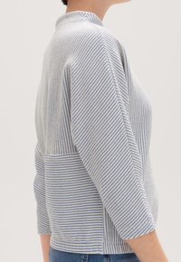 Randig tröja med hög krage, gjord av lätt material; har horisontella blå och vita ränder, trekvartsärmar och en avslappnad passform.