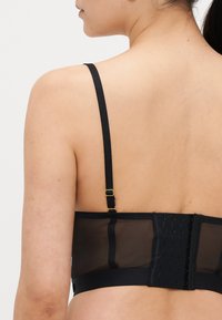 Schwarzer BH mit durchsichtigem Netzrücken, verstellbaren Trägern und goldfarbenen Beschlägen. Verfügt über einen Haken- und Ösenverschluss mit mehreren Einstellungsmöglichkeiten zur Passformanpassung.