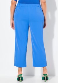 Pantalones anchos azules hechos de un tejido suave con cintura elástica, combinados con zuecos verdes de tacón con un diseño transparente.