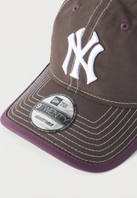 Καφέ και μοβ ρυθμιζόμενο καπέλο μπέιζμπολ New Era με λευκό λογότυπο NY και λεπτομερείς λευκές ραφές στο γείσο.