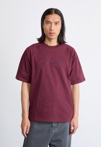Burgunderfarget bomull T-skjorte med rund hals, korte raglanermer og en stor brodert "Carhartt"-logo på framsiden.