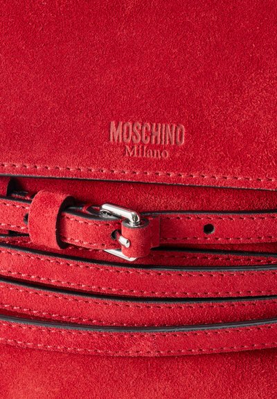 Κόκκινη ζώνη από σουέτ με ασημένια αγκράφα, ραμμένα άκρα και ανάγλυφο λογότυπο "Moschino Milano" στην επιφάνεια του δέρματος.