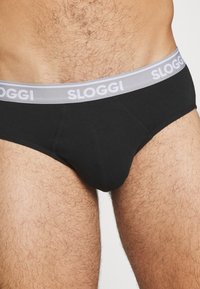 Schwarze Sloggi-Unterhose mit einem grauen Bund, auf dem der Markenname steht. Glatte Textur mit enganliegender Passform und verstärkten Nähten.