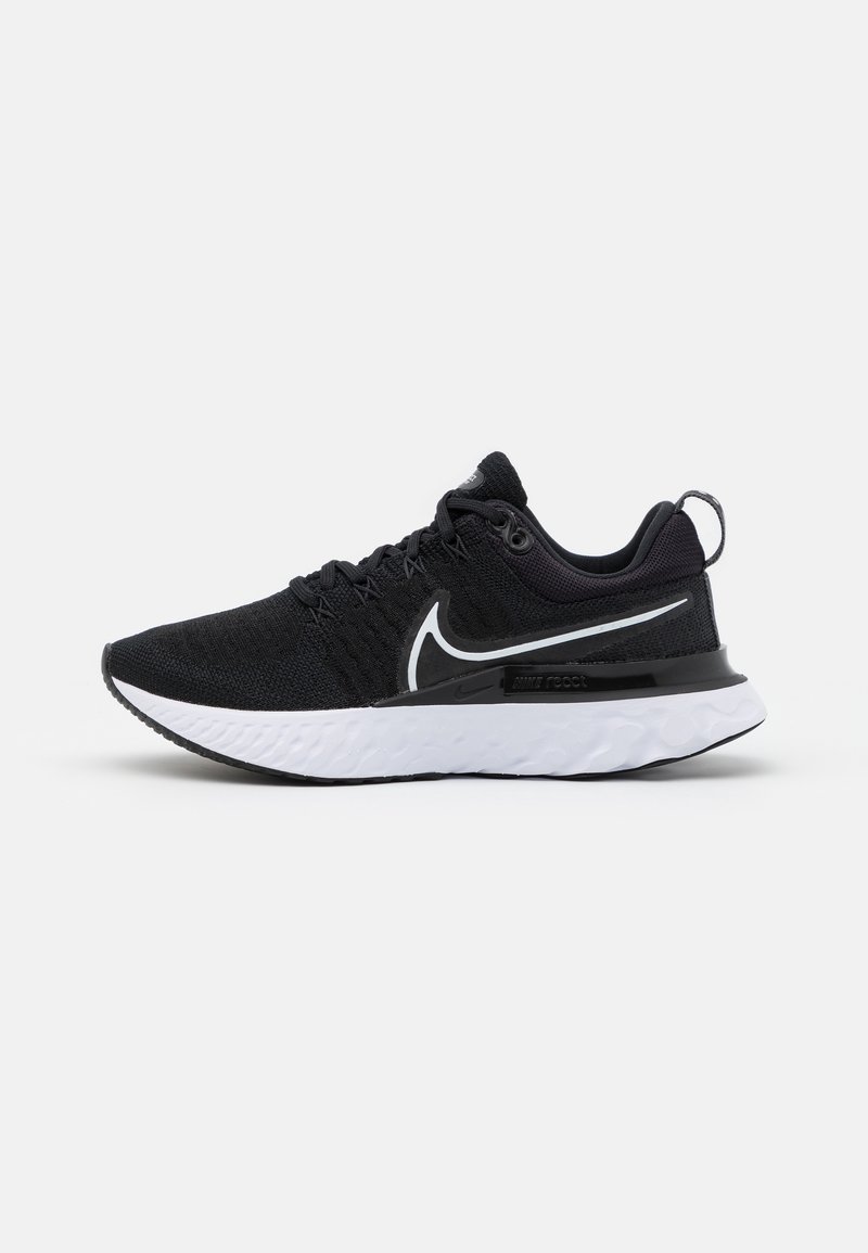 Chaussure de sport noire avec une tige en tissu texturé, semelle intermédiaire blanche, semelle noire et accents réfléchissants. Dispose d'un design à lacets et d'un logo.