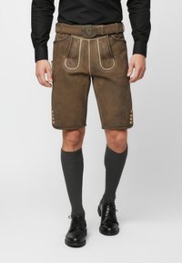 Lederhosen de cuero marrón con costuras decorativas y detalles de ribete en contraste. Presenta botones en los laterales y se lleva con calcetines grises hasta la rodilla.