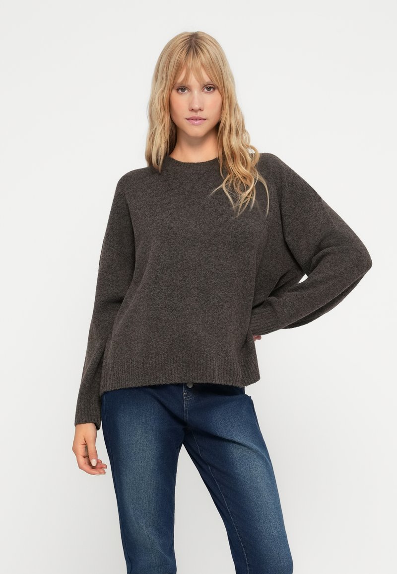 Pull en tricot gris foncé avec un col rond, des épaules abaissées et un ourlet côtelé. Porté sur un jean bleu. Texture lisse.