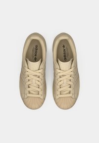 Beige Adidas sneakers with a textured upper, round toe, and traditional lacing. Features prominent brand logo on the tongue and insole.