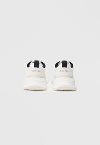 Hvite sportsko med svarte aksenter, med en glatt overdel, polstret krage og en tykk, teksturert såle for grep.