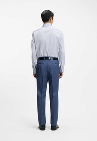 Camicia azzurro chiaro a righe con maniche lunghe e colletto, abbinata a pantaloni blu scuro a righe sottili. La cintura nera e le scarpe completano il look.