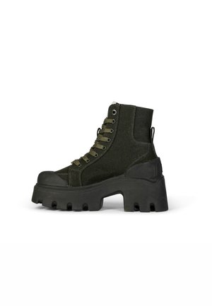 Stivaletto nero realizzato in tessuto texturizzato con suola in gomma spessa, caratterizzato da un design a gradini e occhielli metallici per i lacci.