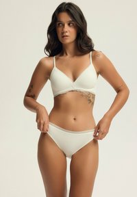 White ribbed bralette with lace trim and adjustable straps, paired with matching bikini brief featuring lace waistband detail.