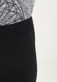 Černé legíny s hladkým povrchem a širokým pasem, doplněné šedým topem s geometrickým černým vzorem.