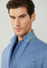 Ljusblå jacka i strukturerad tyg med denimkrage, med slagkrage och bröstficka. Ren, figursydd design.