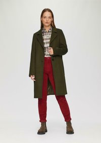 Groene wollen jas, geruite overhemden, rode corduroybroek en bruine enkellaarsjes. De jas heeft een revers en een enkele knoopsluiting.